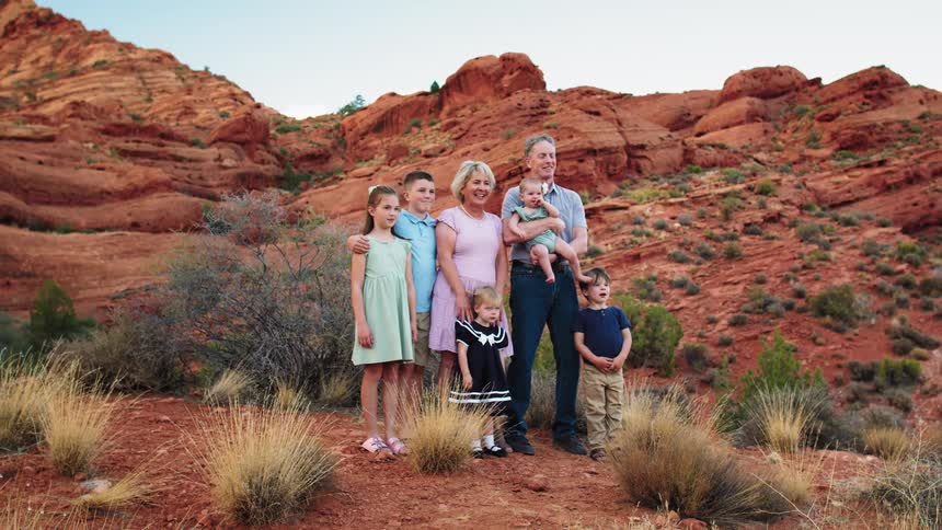 Family poses smiling in front of reddish rock formations under a clear sky