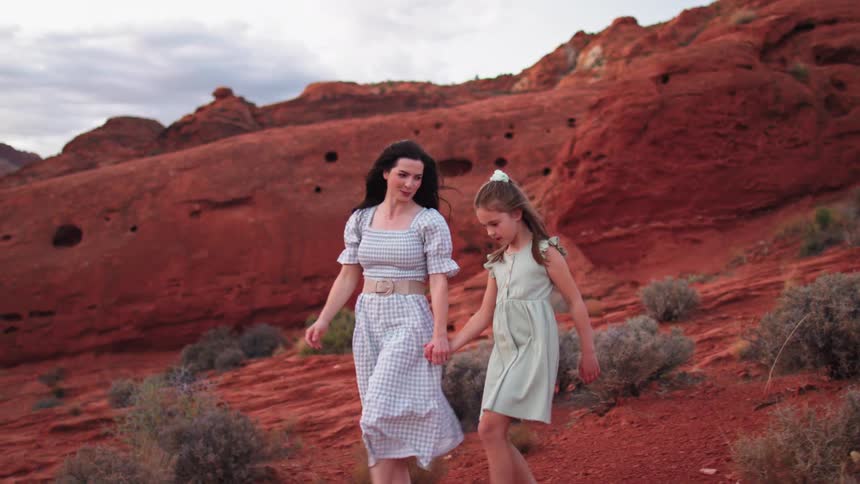 Mother and daughter walk barefoot across red rocky terrain amid striking natural formations
