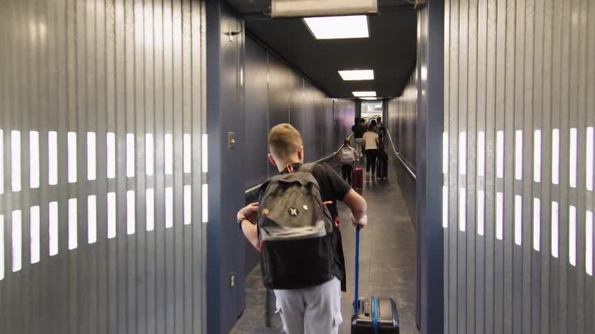 Child walks through the boarding corridor pulling their suitcase