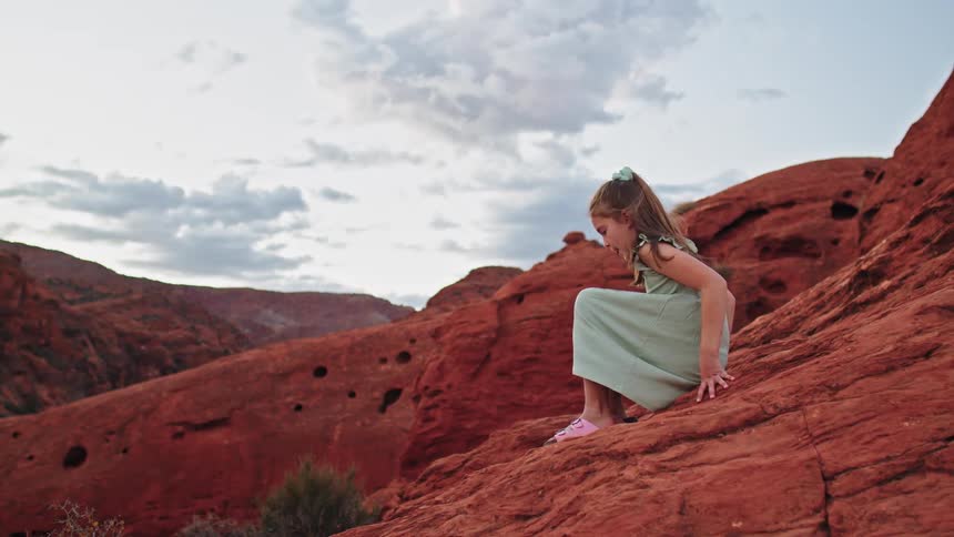 A little girl sitting on a mountain peak gets up and walks down the slope