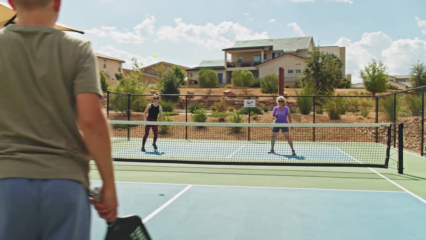 A kid and his father team up in an outdoor tennis match at midday playing energetically against two women as the game unfolds under the bright sun