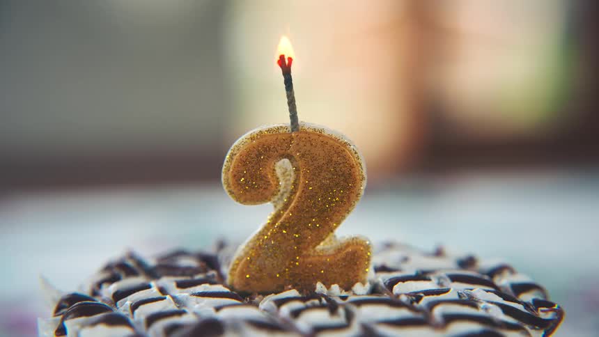 Golden number two candle lit on a decorated cake