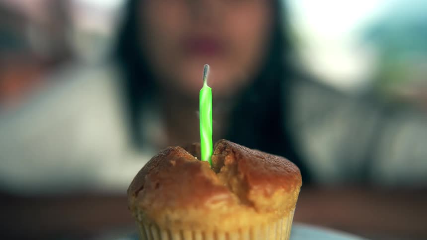 Woman blows out candle on a cupcake with smoke slowly rising