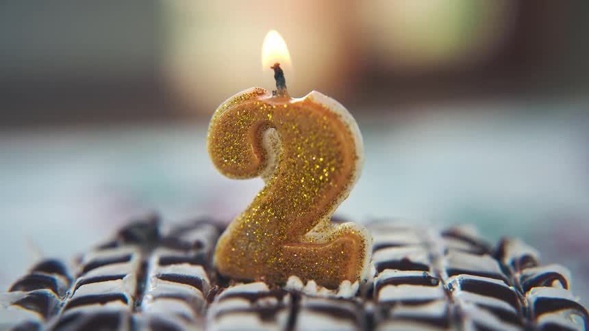 Golden number two candle burning on a cake topped with icing