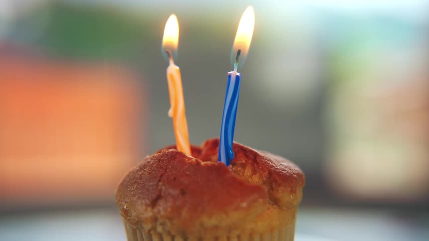 Two lit candles stand on a brown cake their flames flickering before both are blown out leaving a wisp of smoke curling into the air