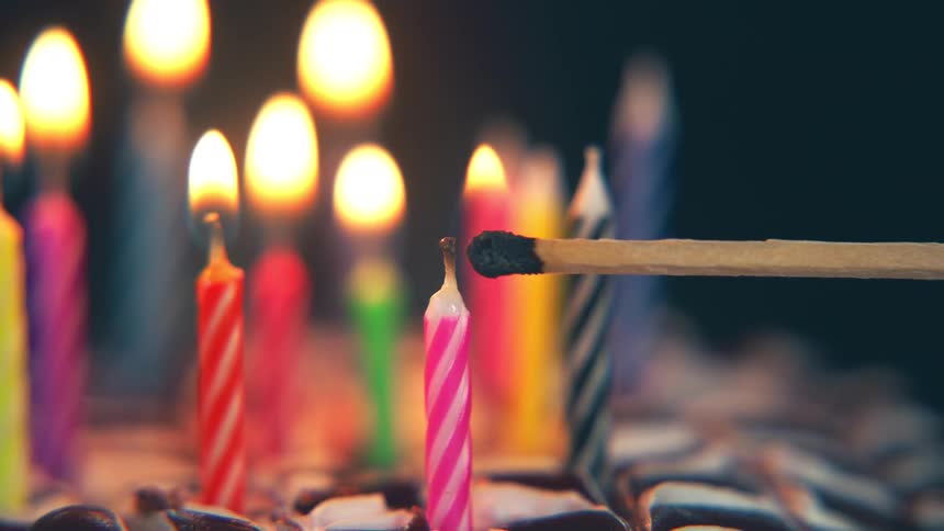Extinguished matchstick in front of lit colorful candles on a cake