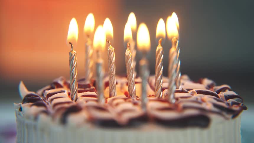 A birthday cake topped with rich chocolate icing is decorated with multiple candles their flames glowing brightly as they light up the cake