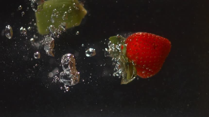 A strawberry and piece of kiwi are dropped into water and sink