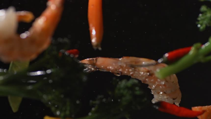 Several vegetables and shrimp float in a black space