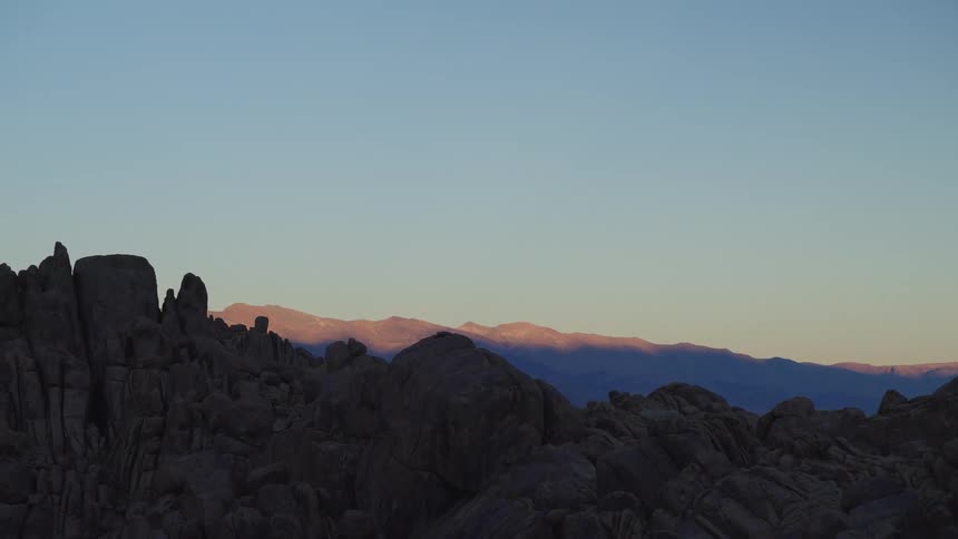 Golden sunset light illuminates a distant mountain range above dark rock formations
