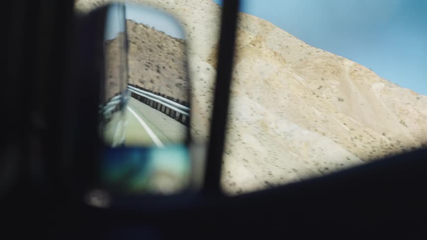A desert highway curves through rocky hills reflected in a cars side mirror