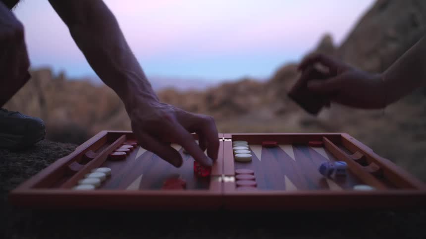 Two people play a board game outdoors at midday