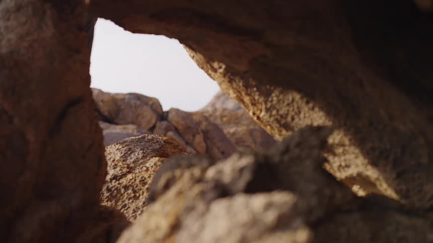 Person climbs rocks under sunlight seen through a crevice