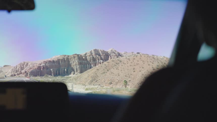 A woman sits in the passenger seat of a car during a road trip in the countryside at midday