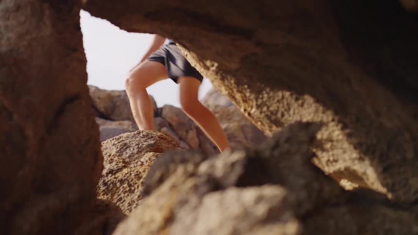 Person climbs between sunlit rocks seen through a crevice