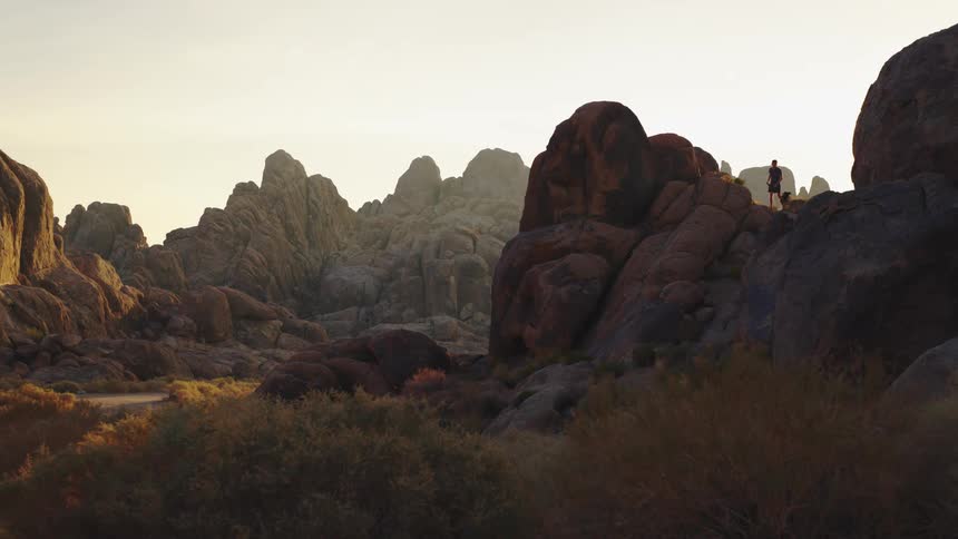 A man runs on a rocky formation with a dog on a leash on a sunny day