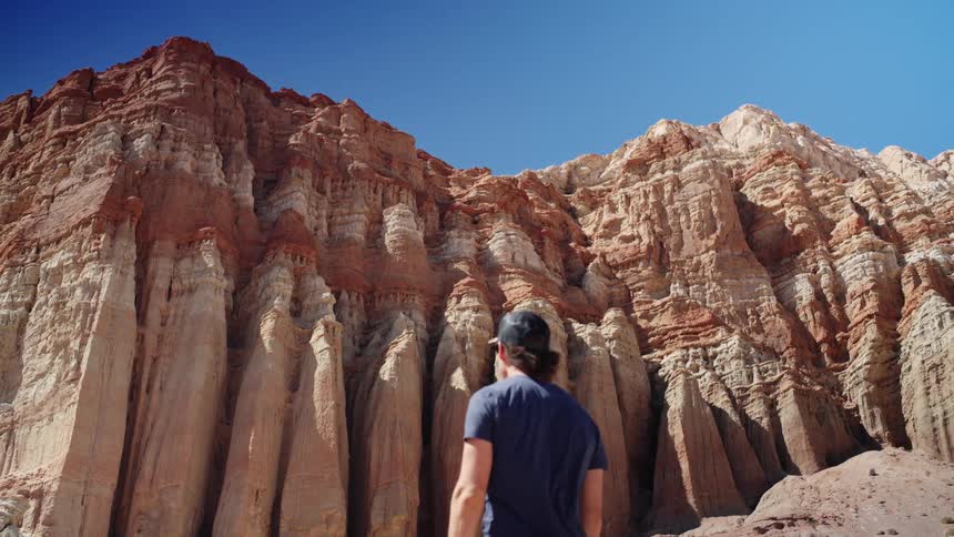 A man walks up to the side of a mountain and looks up at it