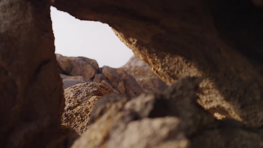 A man hikes across rocky terrain at midday dressed in shorts