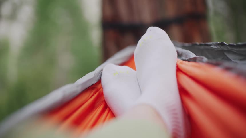 Person lying in orange hammock with white socks facing tree trunk secured by black strap