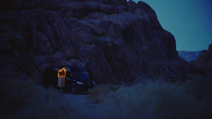 Van parked among rocks glows with warm interior light at dusk