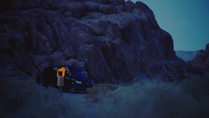 A man and a woman outdoors walking toward a van near a mountain and then getting into the van