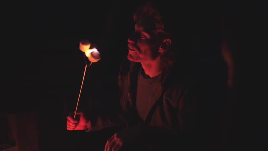 A man laughs as he roasts a marshmallow that catches fire