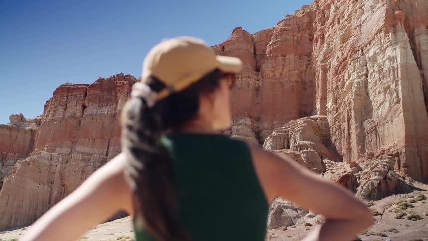 A woman standing with her hands on her hips observing a canyon
