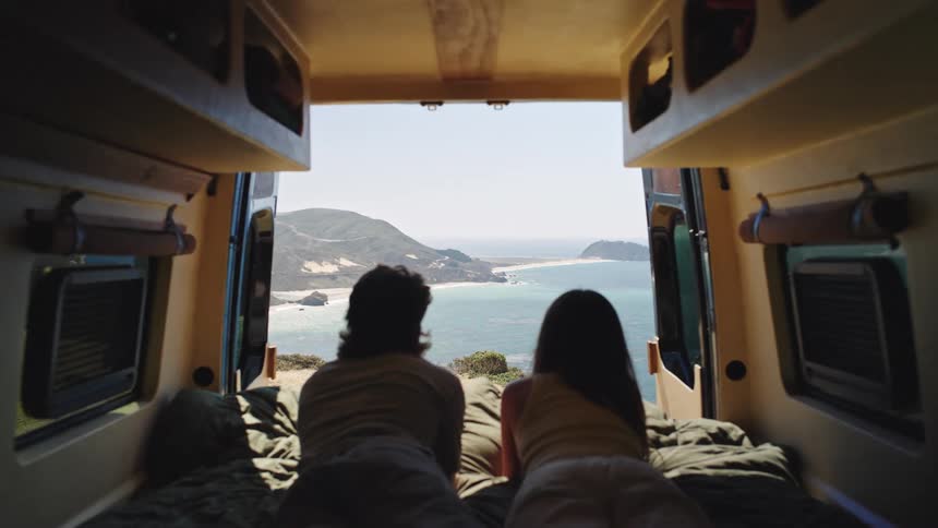 Couple lying at the back of a camper van gazing at ocean cliffs