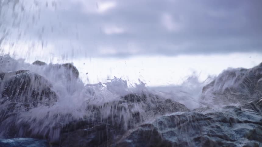 A powerful ocean wave crashes dramatically over wet rocks on the shore