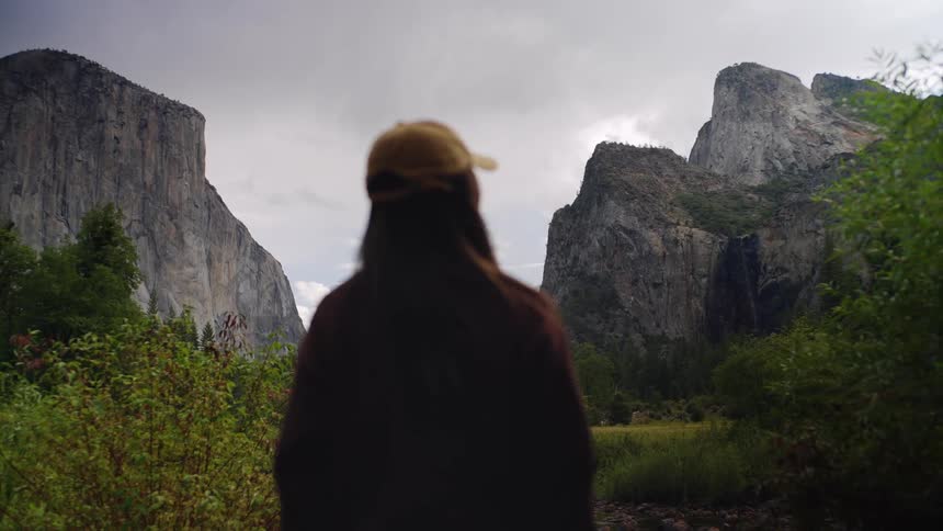 Person wearing a cap observing rocky mountains covered with greenery