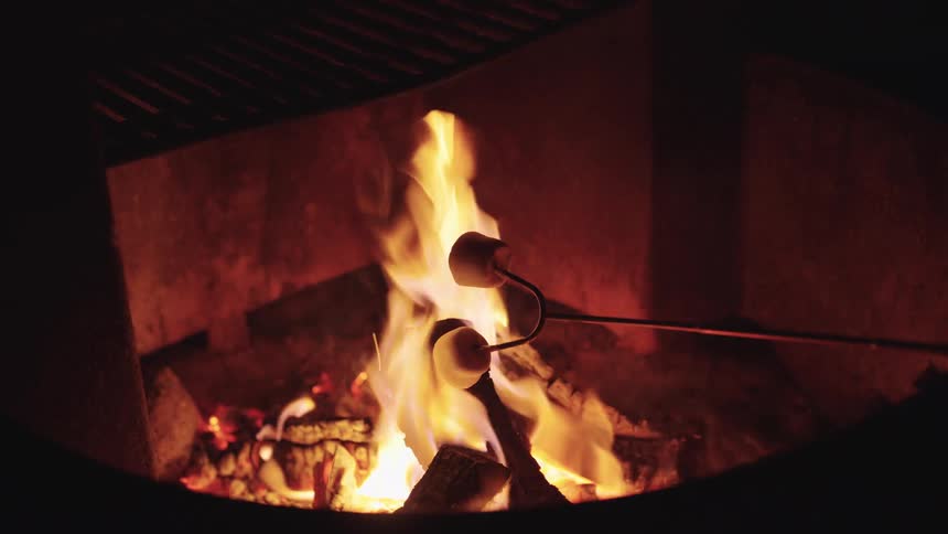 A closeup of marshmallows roasting over a glowing campfire in the dark