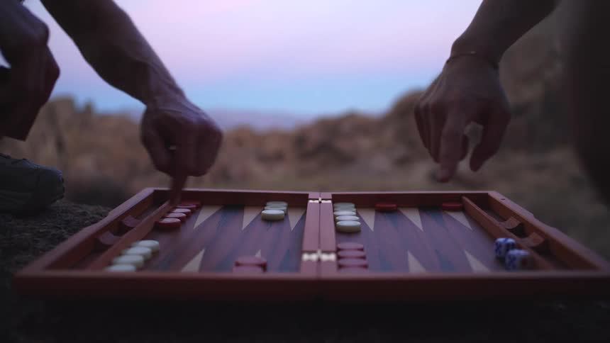 Backgammon game in progress on rocky surface with mountains in the background at sunset