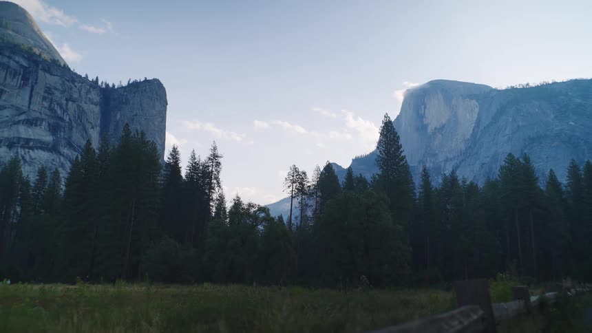 A scenic view of towering granite cliffs rise above pine trees in a clear mountain valley
