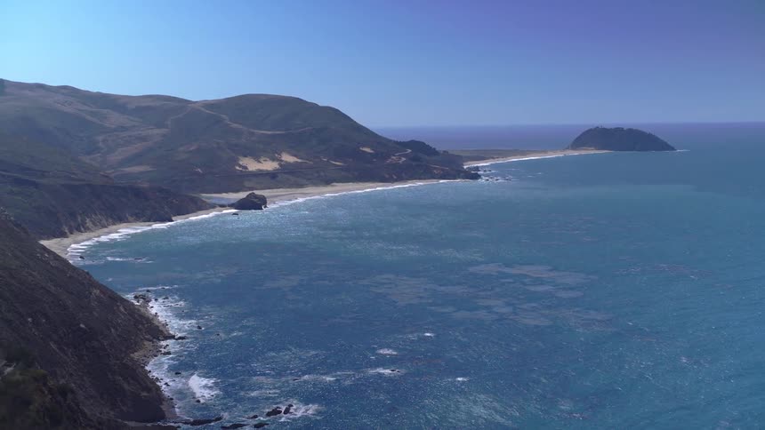 Waves roll onto a beach that is surrounded by mountains