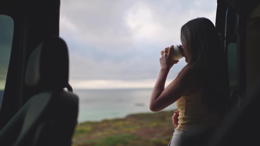 A woman is standing in the side door of her caravan looking as the storm rolls in over the coast