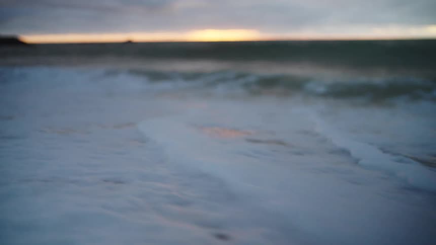 Gentle waves wash onto a sandy beach at sunset under a cloudy sky