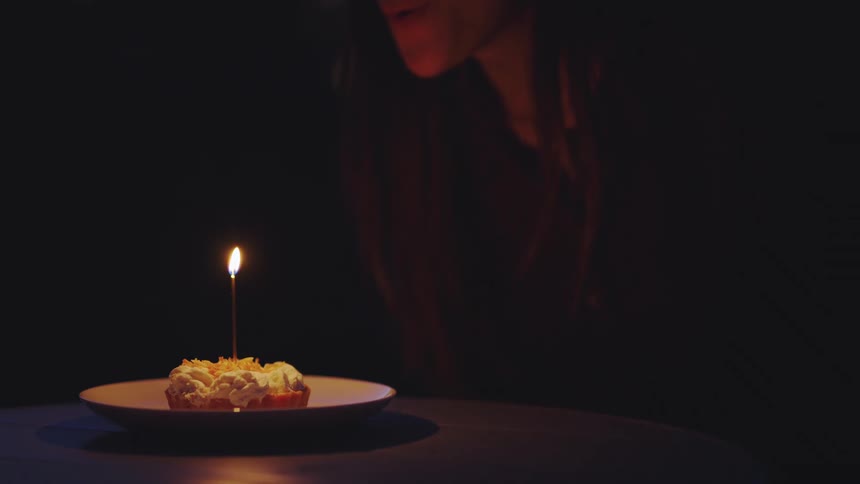 A person blows out a candle on a small dessert in a dark room