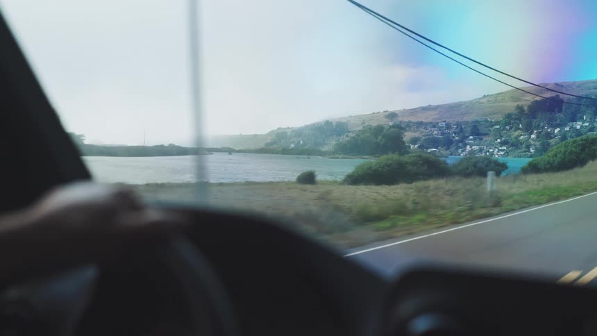 A person holds a steering wheel while driving in the countryside at midday