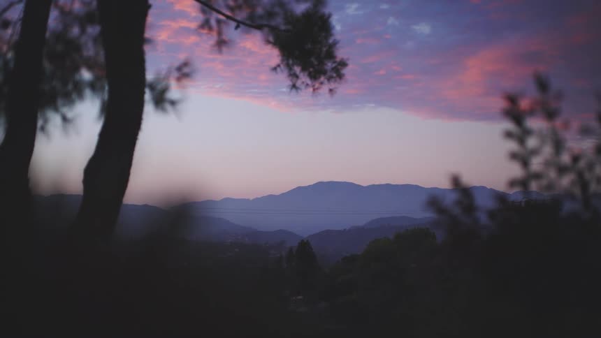 A scenic view shows tree covered hills under a colorful dusk sky