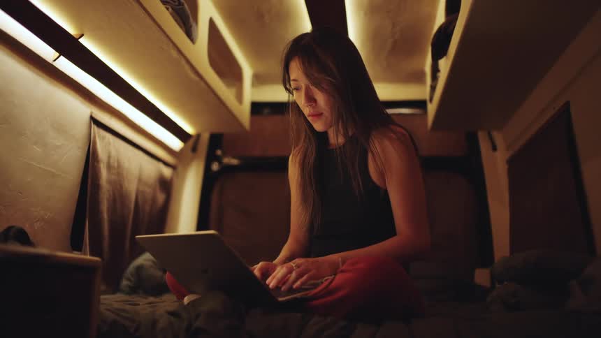 A woman is sitting in her caravan typing on a laptop