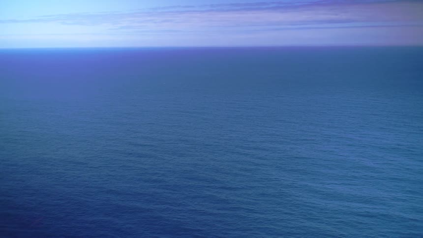 Blue horizon stretches over the calm sea beneath a partly cloudy sky