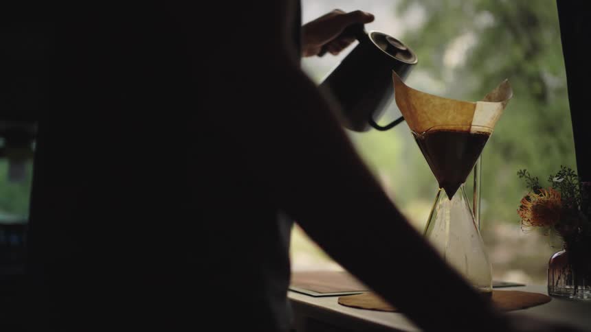 The man pours hot water into the filter over the pitcher