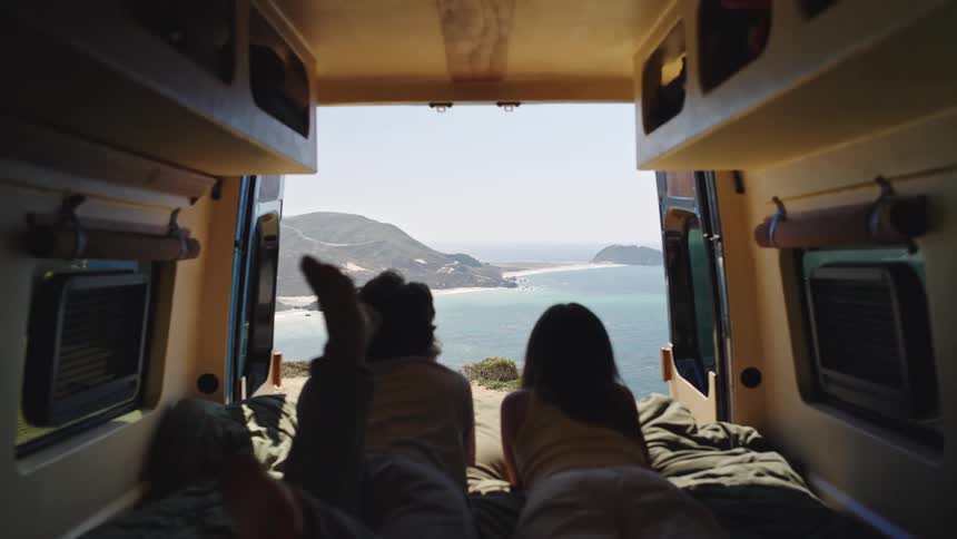 People are laying in bed in their caravan looking out at the beach and mountains