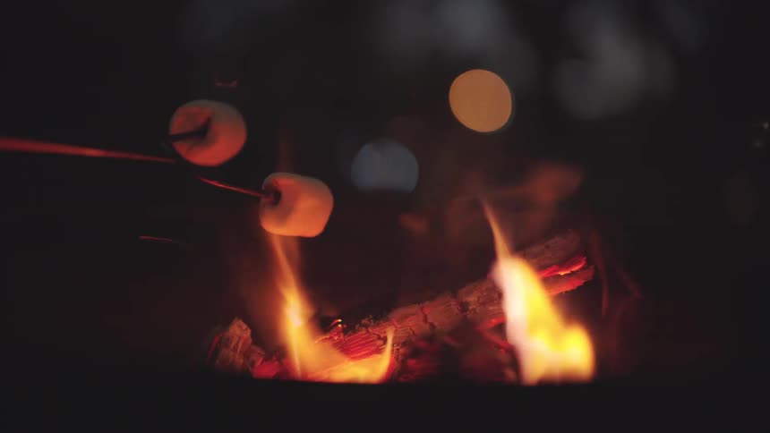 Closeup of marshmallows on a stick being roasted over a campfire at night