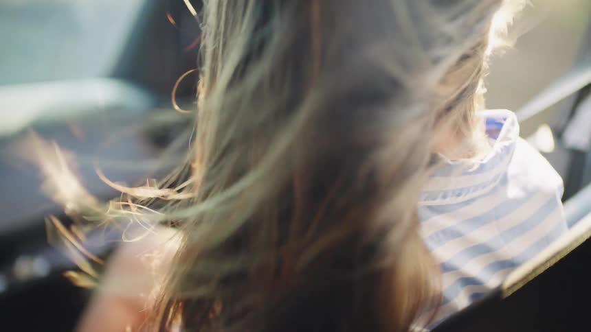 The window is down in a car and makes a womans hair move as the car drives