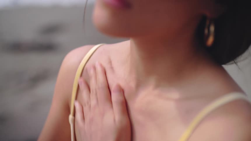 Woman gently touches her chest while looking toward the horizon