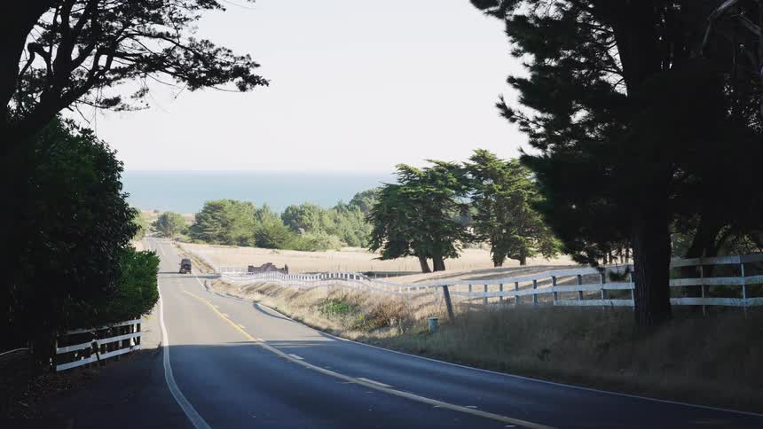 A van drives on a freeway in the countryside with trees lining both sides of the road on a sunny day