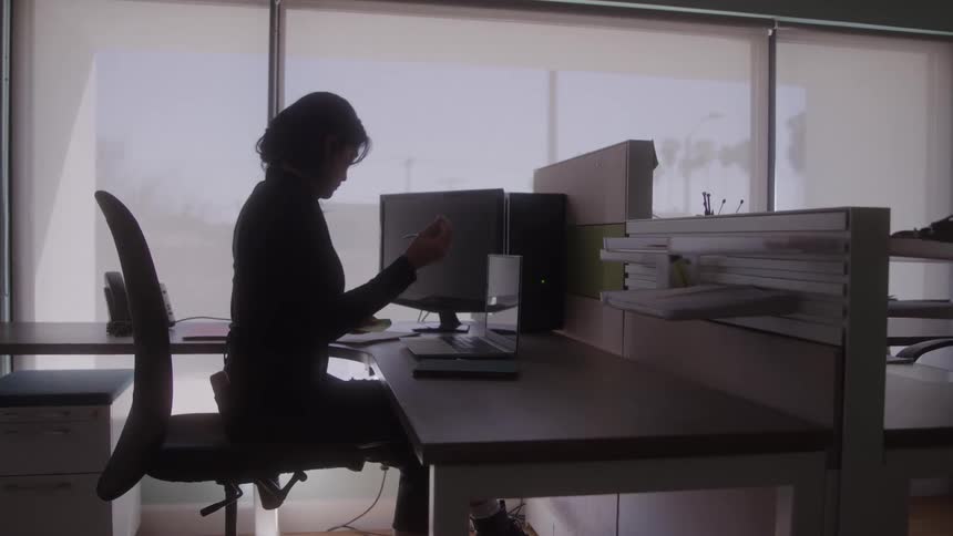 A woman reaches across her desk for a pen in a bright modern office
