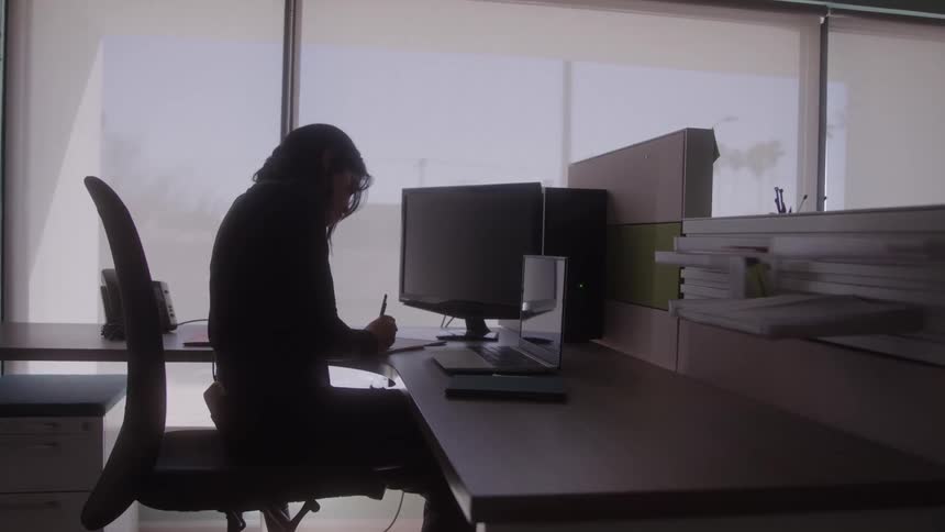 A woman sitting on a chair in an office writing on a piece of paper