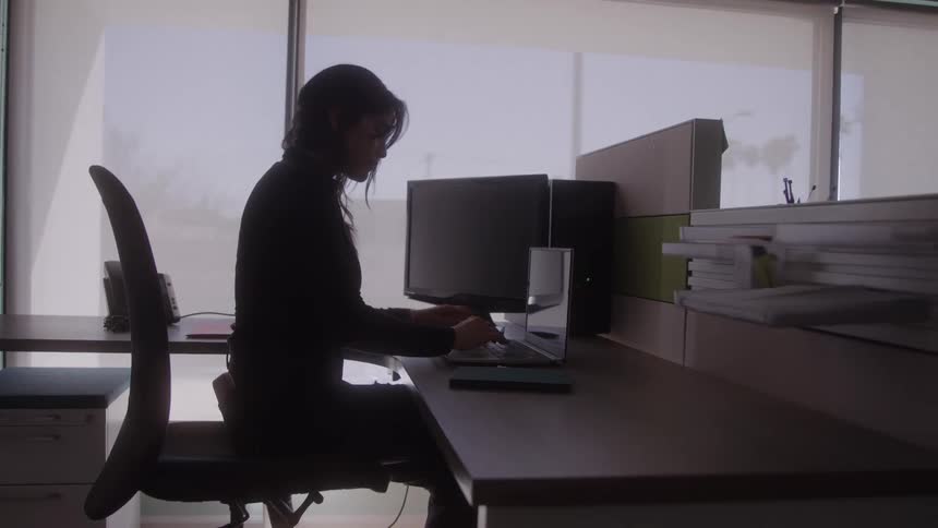 A woman works alone on her laptop in a softly lit modern office